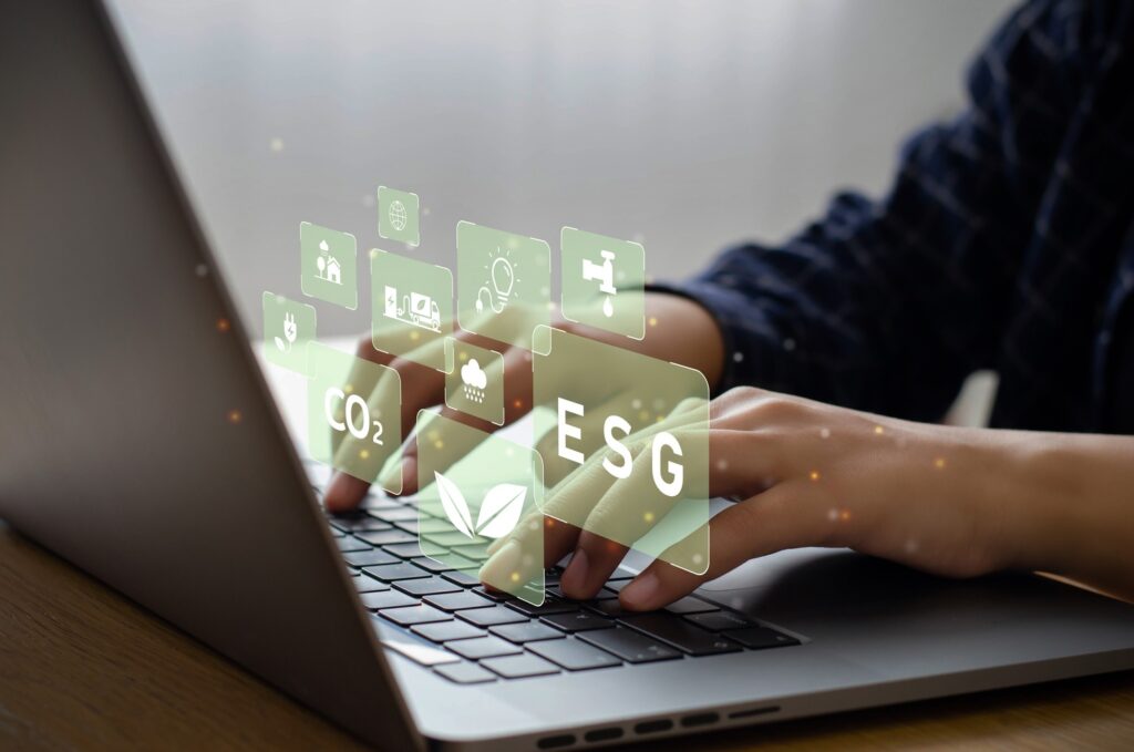 A person types on a laptop with floating icons related to environmental, social, and governance (ESG) criteria, including CO2, renewable energy, and social responsibility.