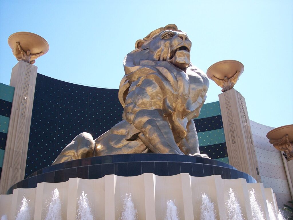 A large golden lion statue sits atop a building entrance with ornate columns and fountains in front.