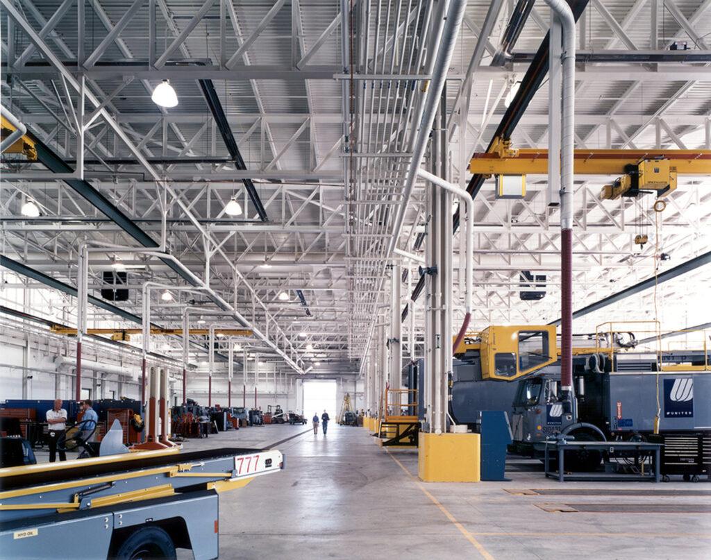 Interior of a modern, spacious industrial facility with high ceilings, showing various machinery, equipment, and a few workers in the distance.