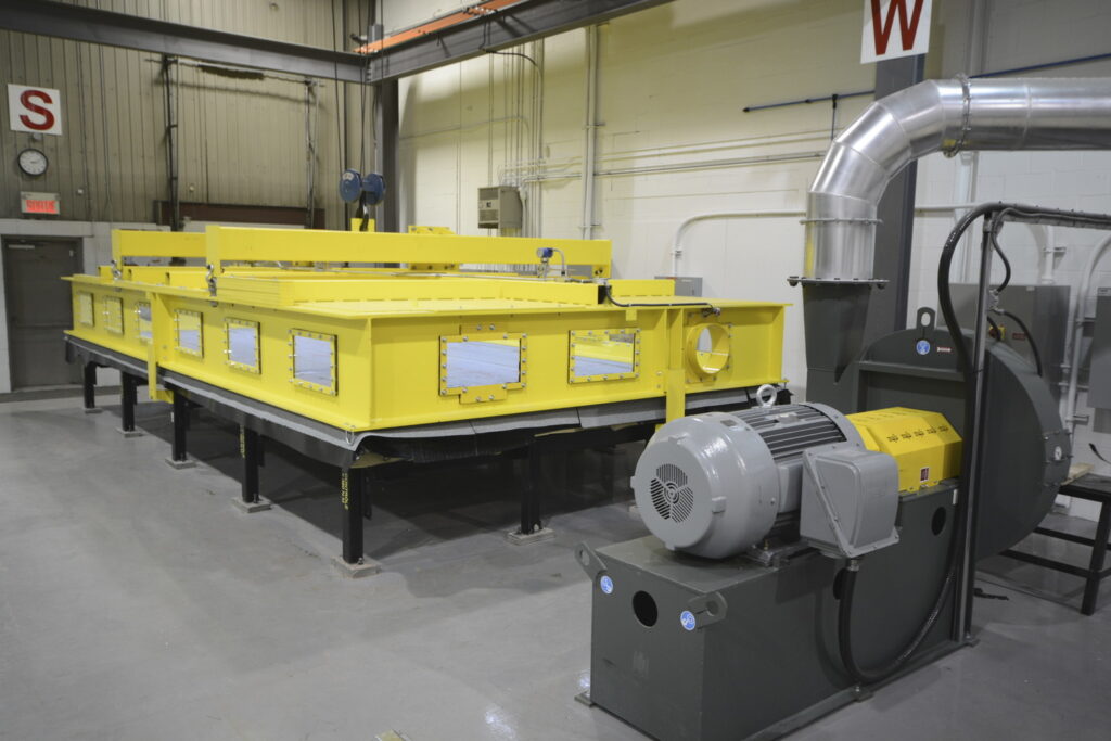 Industrial machinery in a factory setting, featuring a large, yellow rectangular unit on black legs connected to a gray motor unit with ducts.