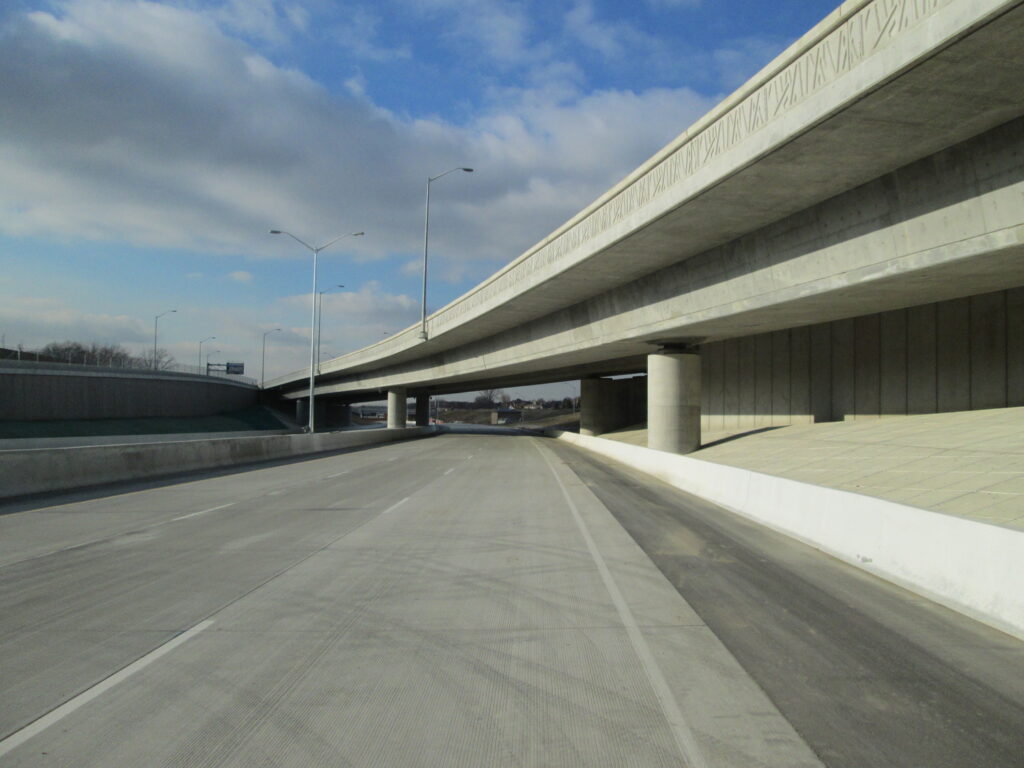 An empty highway with two overpasses on a clear day under a partly cloudy sky.