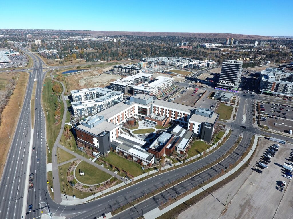 Aerial view of a large modern building complex surrounded by roads, with a mixture of commercial and residential areas in the background, set against a clear sky.