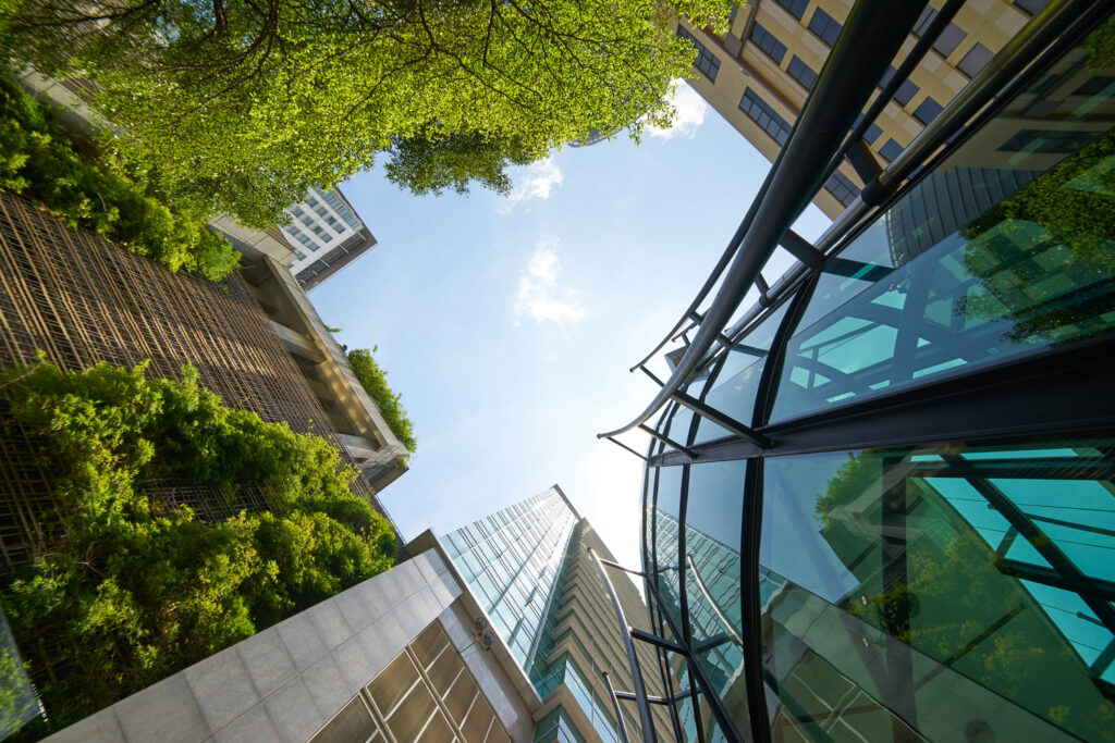 Low-angle view of modern urban buildings with greenery visible on some facades and a blue sky with scattered clouds above.