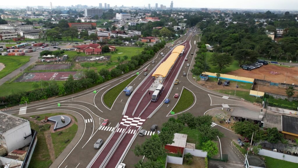 Aerial view of a multi-lane urban road with a central bus rapid transit station, vehicles, and surrounding greenery and city buildings in the background.