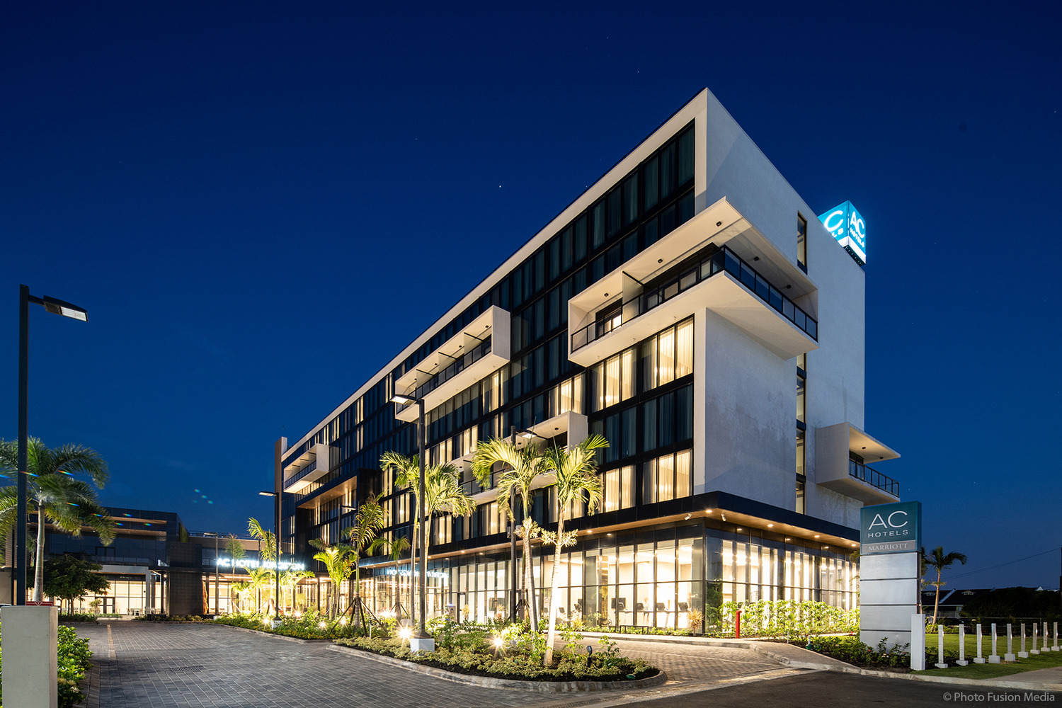 Night view of a modern multi-story hotel with illuminated windows and palm trees lining the entrance.