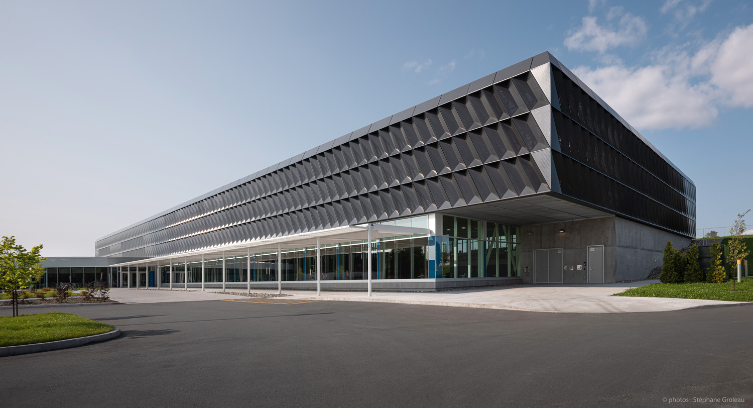 Modern building with angular architectural design, featuring a large glass entrance and a paved outdoor area under a blue sky.