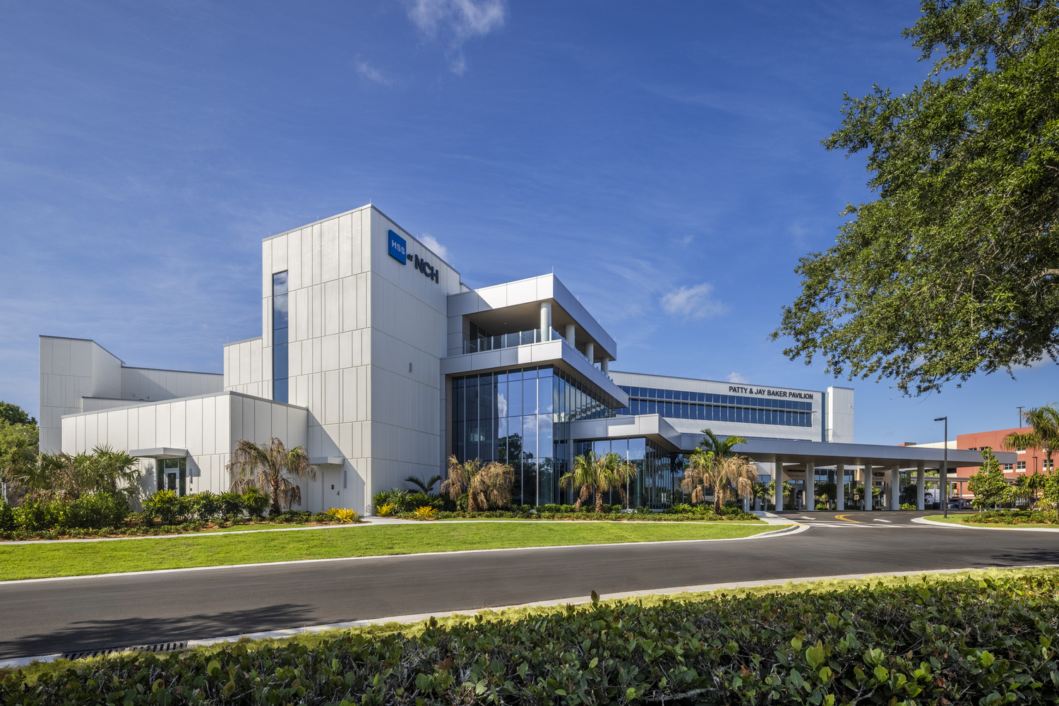 Modern multi-story medical building with glass and white exterior, landscaped grounds, and clear blue sky in the background.