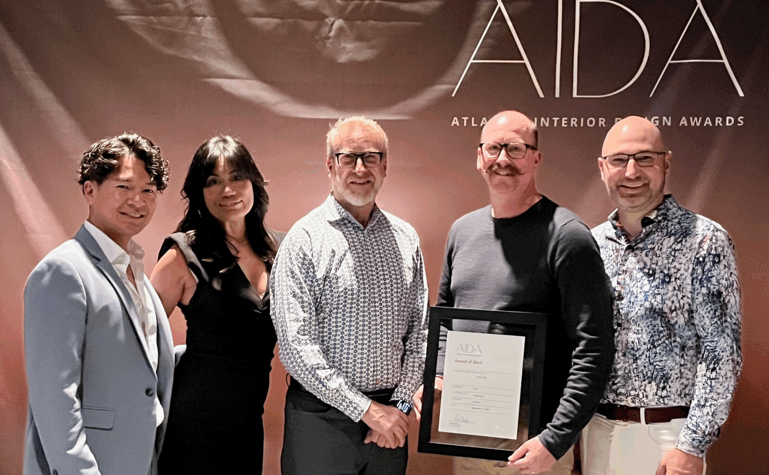Five people stand in front of an AIDA banner; one man in the center holds a framed award certificate.