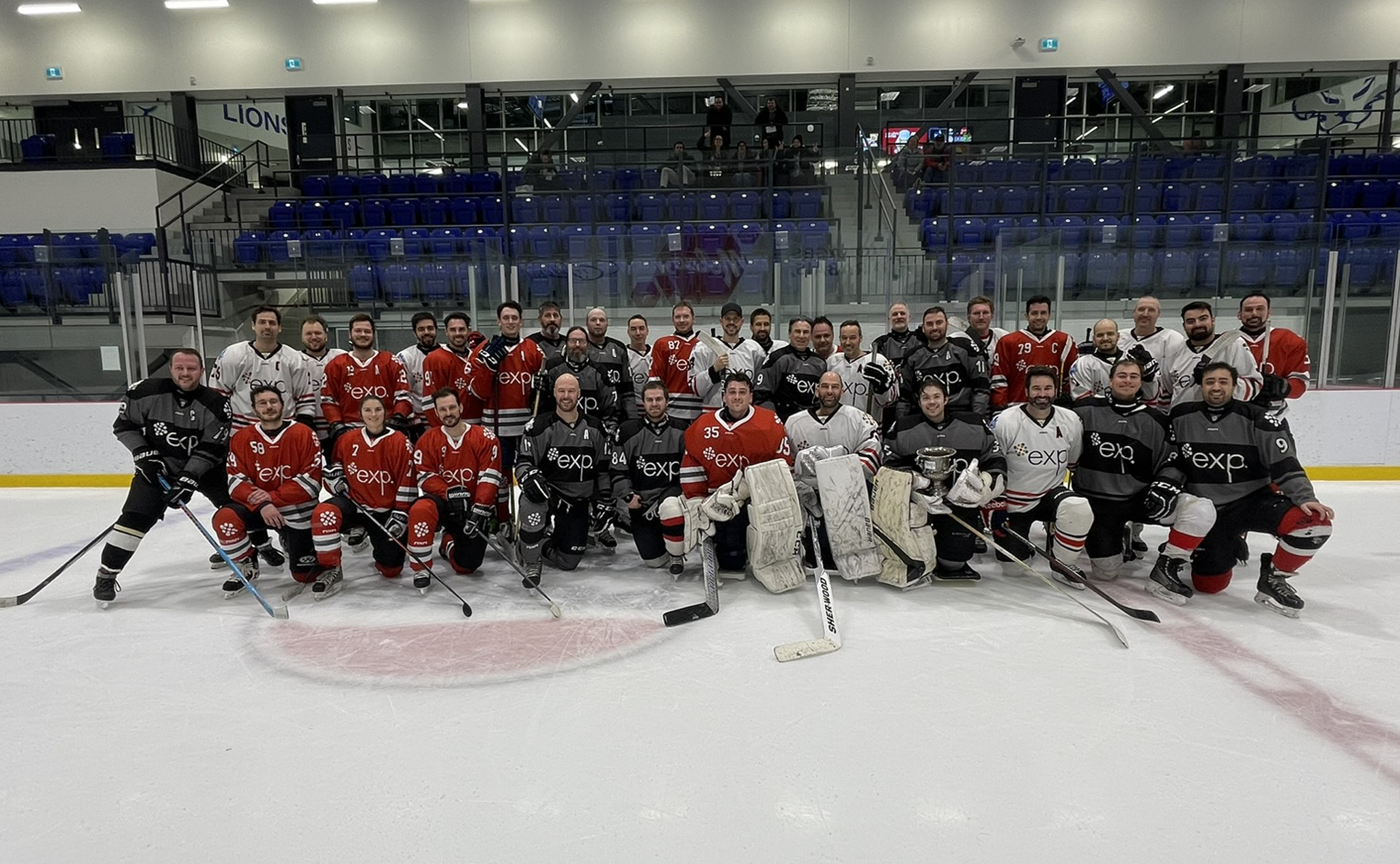 A group of hockey players in red and black jerseys pose for a photo on an ice rink inside a sports arena.