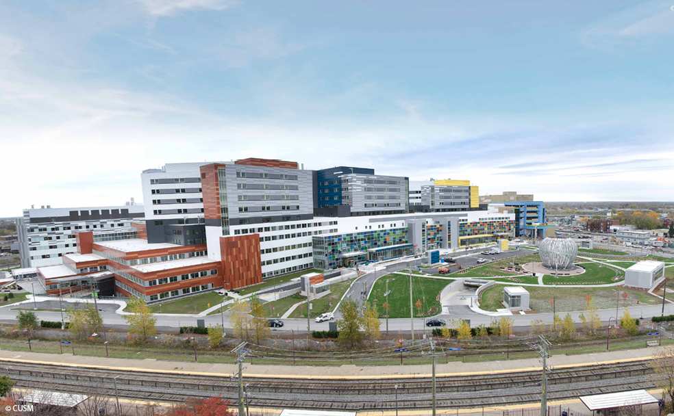 A large, modern hospital complex with multiple connected buildings and landscaped grounds under a cloudy sky.