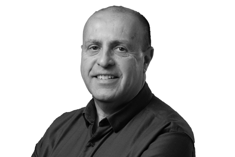 Man smiling at the camera in a black and white portrait, wearing a dark button-up shirt.
