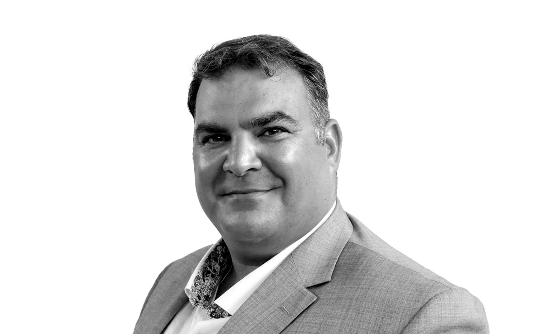 A man in a suit jacket and collared shirt smiles at the camera against a plain white background.