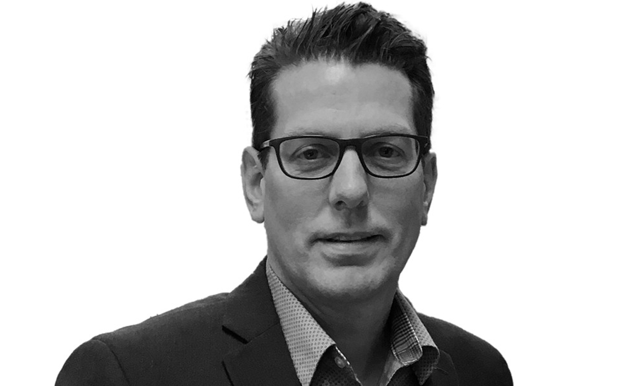 A man with short dark hair and glasses, wearing a suit jacket and checkered shirt, poses against a plain white background.